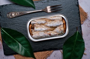 Closeup of can of sardines in olive oil on a black slate stone,view from above.